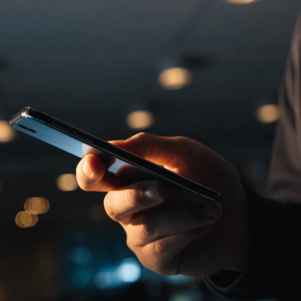 Hands holding a phone in a dark room, the display reading as a dark glass plane